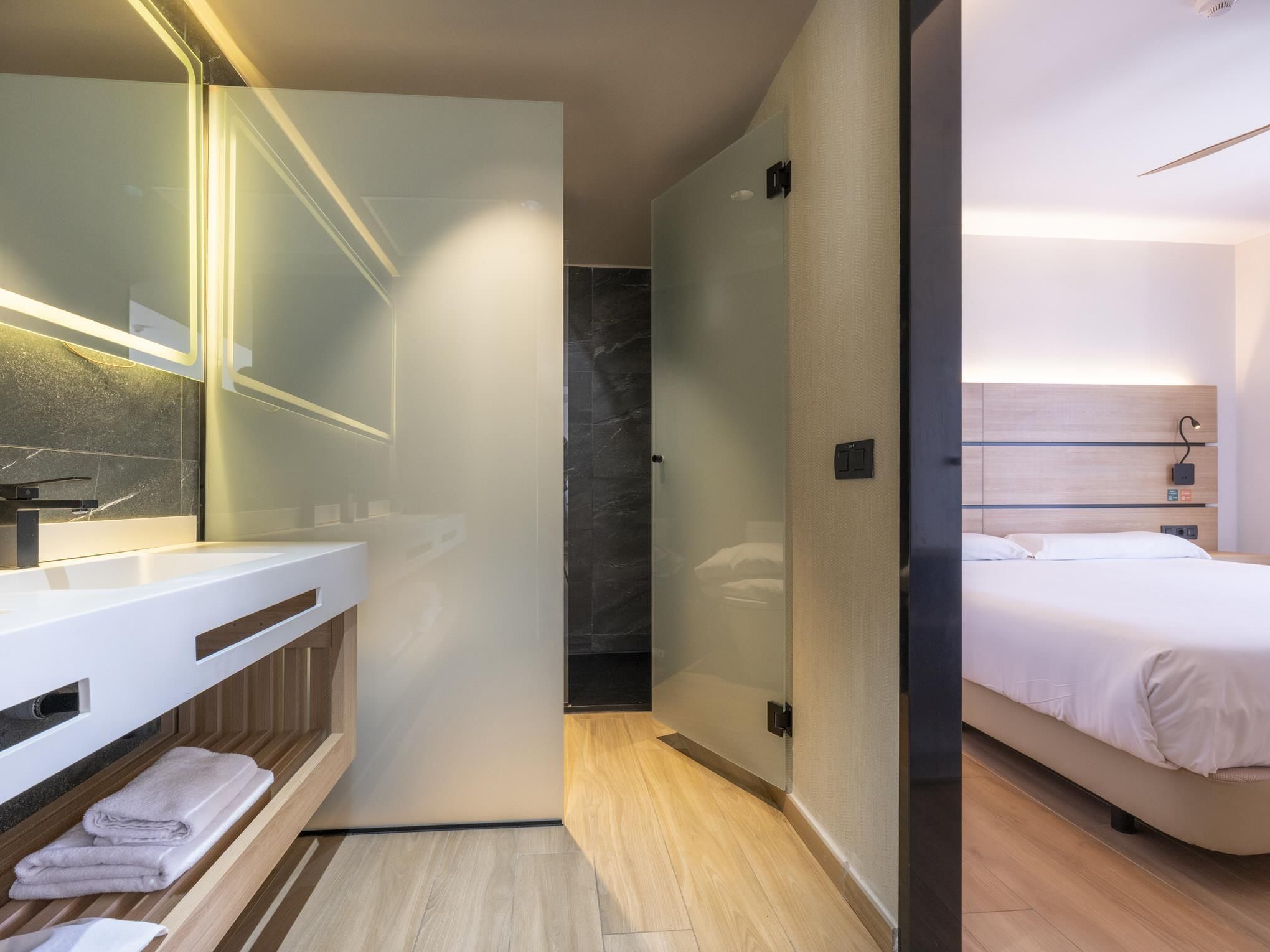 Une chambre d’hôtel moderne avec salle de bain, un lit et un grand miroir.