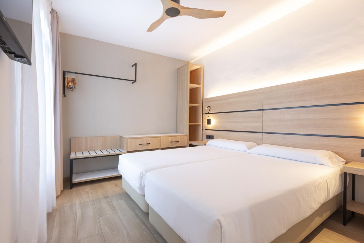 A modern hotel room with a large bed, a desk, a wardrobe, and a ceiling fan.