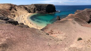 A beach with clear turquoise waters, rocky cliffs, and a dirt path leading to the shore. - MYND Yaiza (Yaiza)
