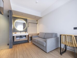 A modern room with a grey sofa, a round mirror, a wooden floor, and a wicker chair. - MYND Yaiza (Yaiza)