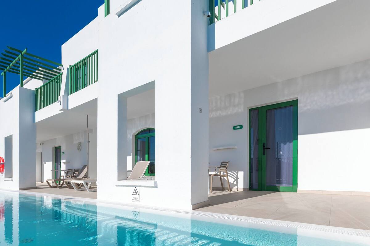 A modern hotel with a swimming pool, outdoor seating, and a green door.