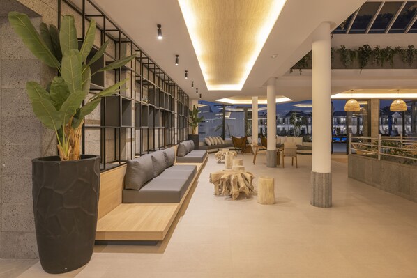 A modern interior with a long sofa, wooden tables, and a large potted plant. - MYND Yaiza (Yaiza)