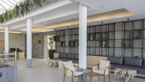 A spacious lobby with a modern design, featuring a seating area with wooden chairs and a sofa, a large wall with shelves, and a ceiling with skylights. - MYND Yaiza (Yaiza)