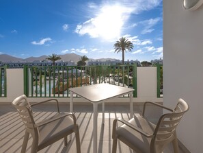 A balcony with a table and chairs, overlooking a pool and buildings with mountains in the background. - MYND Yaiza (Yaiza)