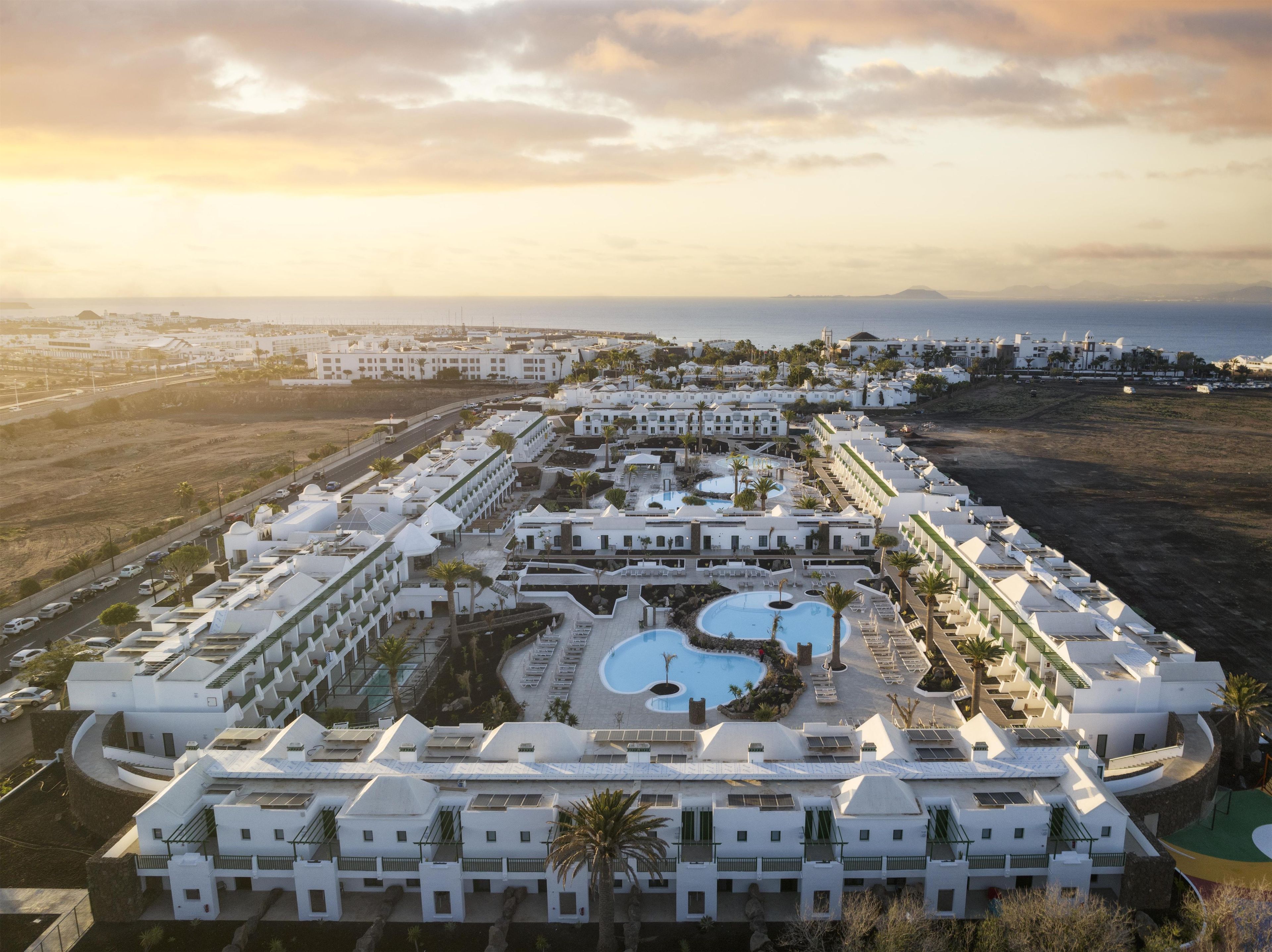 Un resort con varias construcciones, una zona de piscina central y vistas al mar.