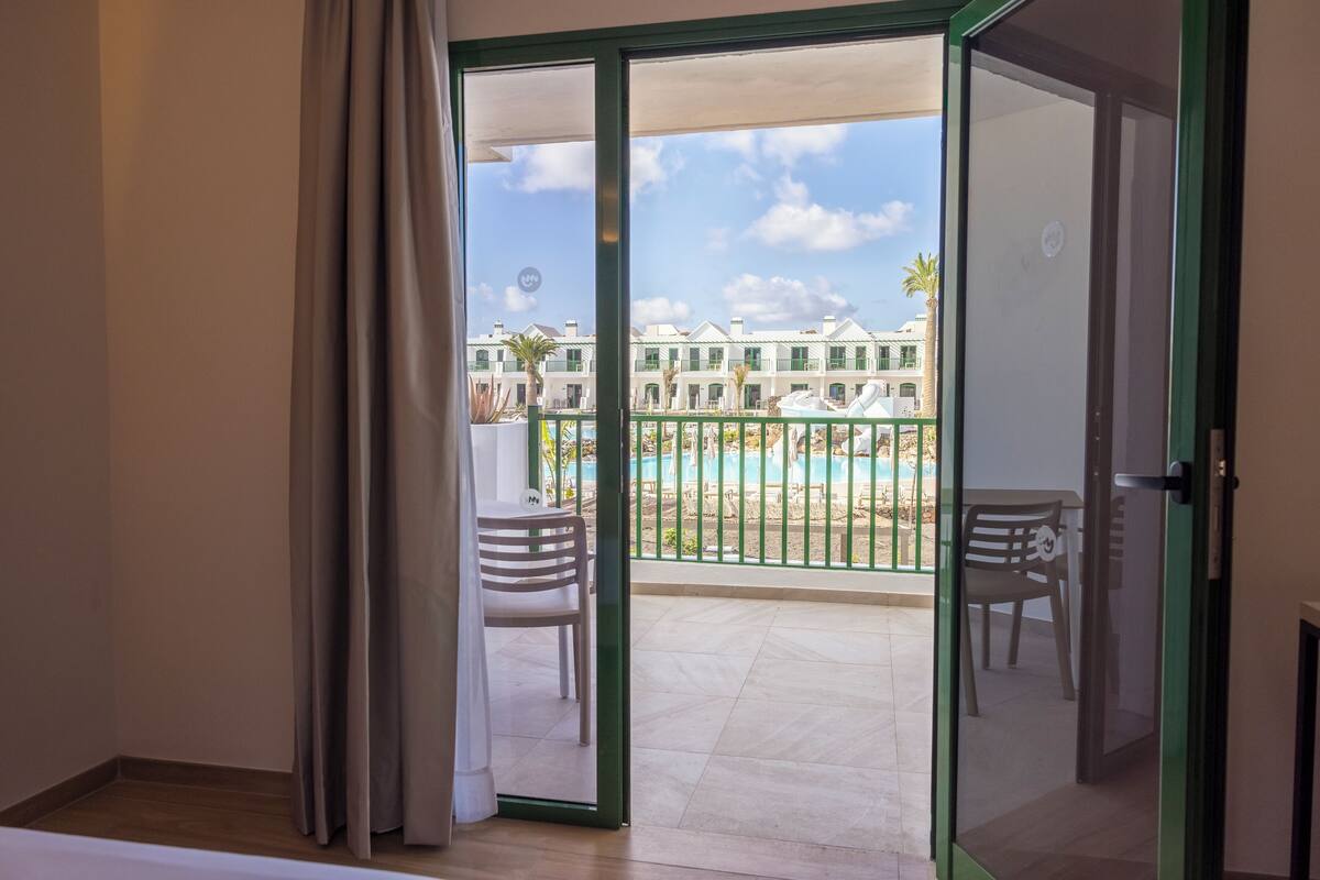 A room with a sliding glass door leading to a balcony with a pool and outdoor seating.