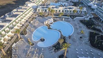 Ein Resort mit mehreren Swimmingpools, Liegestühlen und Palmen.