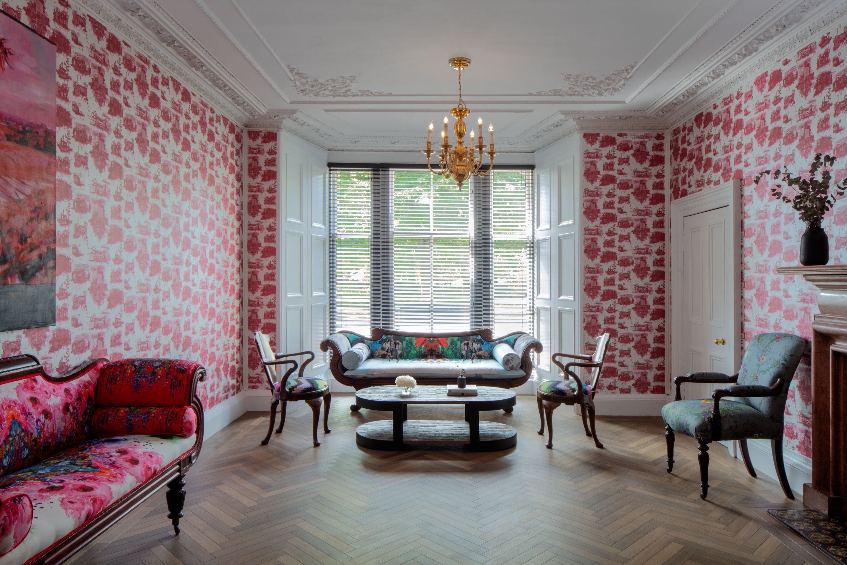 A room with a patterned wallpaper, a sofa, chairs, a coffee table, and a chandelier.
