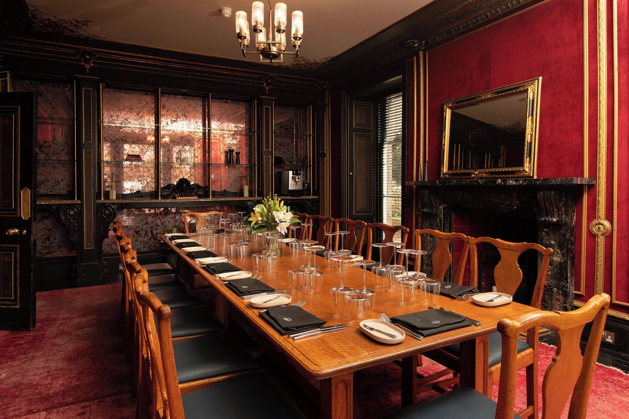 A formal dining room with a long table set for a meal, wooden chairs, a chandelier, and a fireplace.