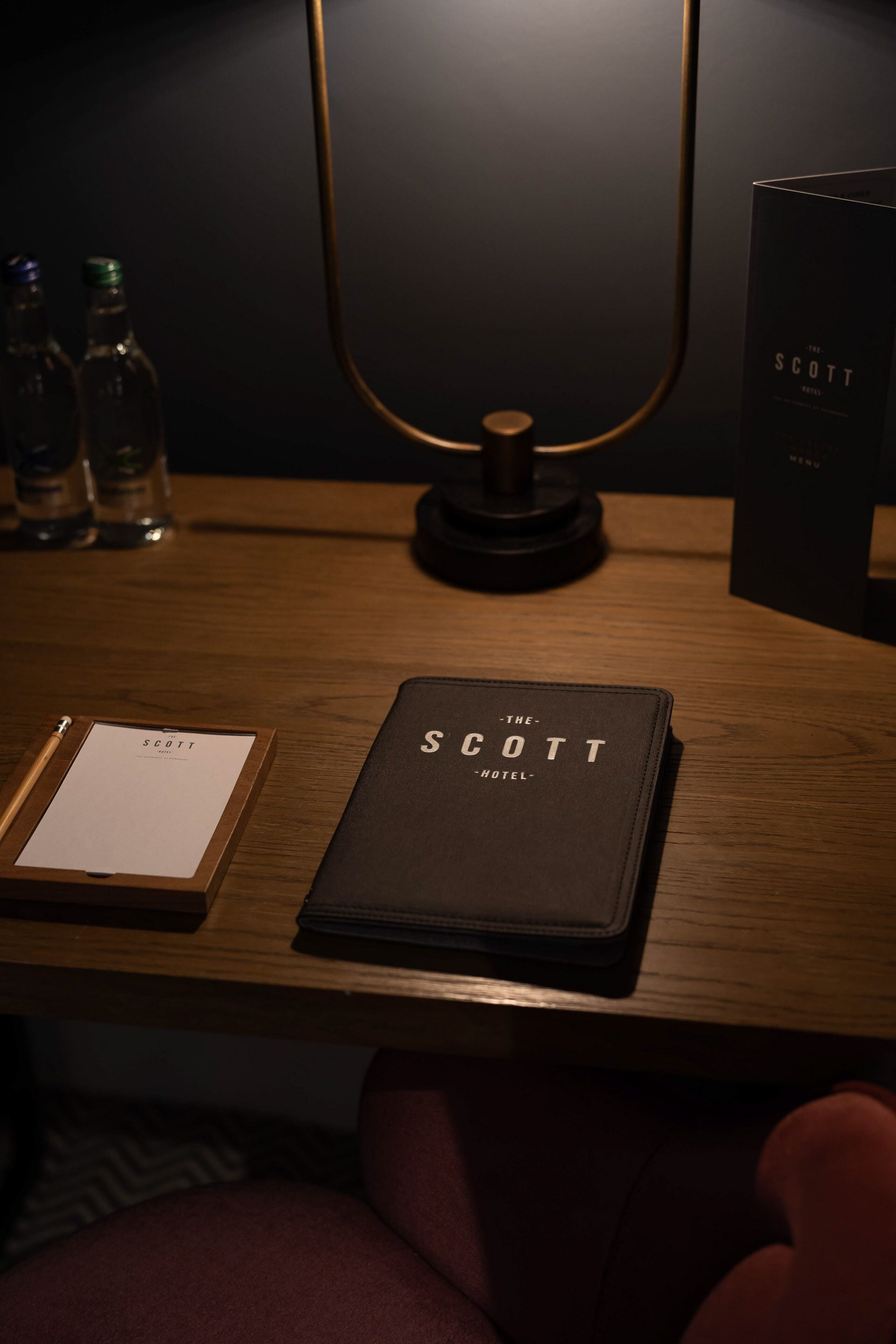 A wooden desk with a lamp, a notebook, and a book titled "The Scott Hotel."