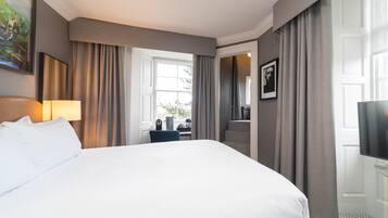 Habitación de hotel con una cama grande, un escritorio con silla, televisor y ventana con cortinas.