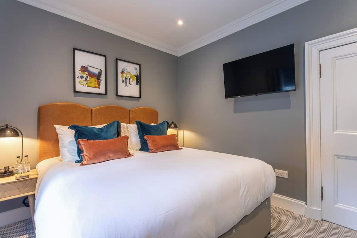 Ein Hotelzimmer mit einem großen Bett, einem wandmontierten Flachbildfernseher und zwei gerahmten Kunstwerken über dem Bett.