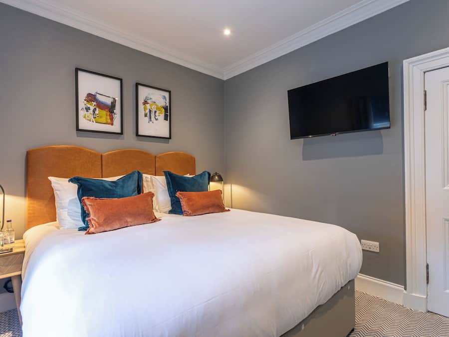 Une chambre d’hôtel avec un grand lit, un téléviseur à écran plat fixé au mur et deux œuvres d’art encadrées au-dessus du lit.
