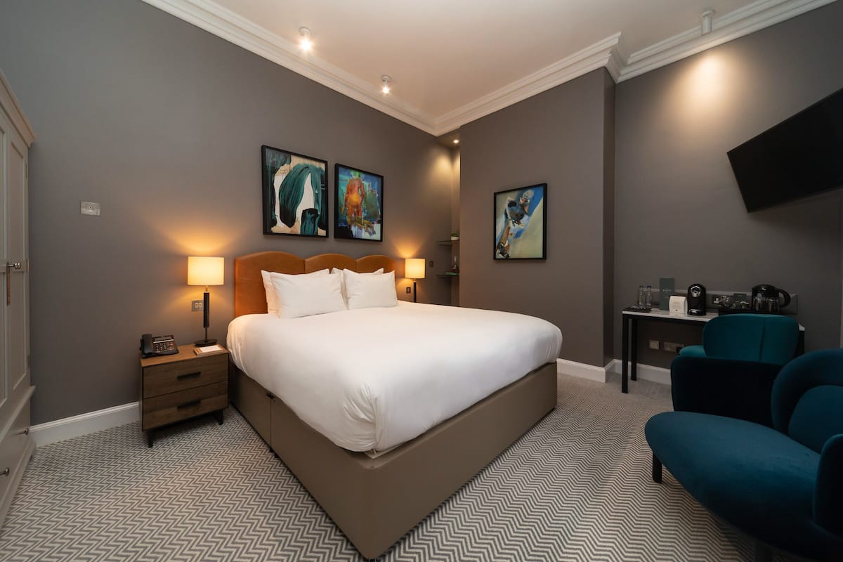 Ein Hotelzimmer mit einem großen Bett, Nachttischlampen, einem Schreibtisch mit Stuhl und Bildern an den Wänden.