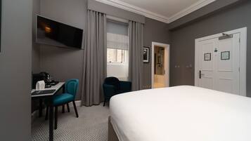 Una habitación de hotel con una cama, un escritorio con una silla, un televisor montado en la pared y una puerta con un letrero.