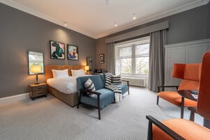 A modern hotel room with a large bed, a sofa, a chair, and a window with curtains.