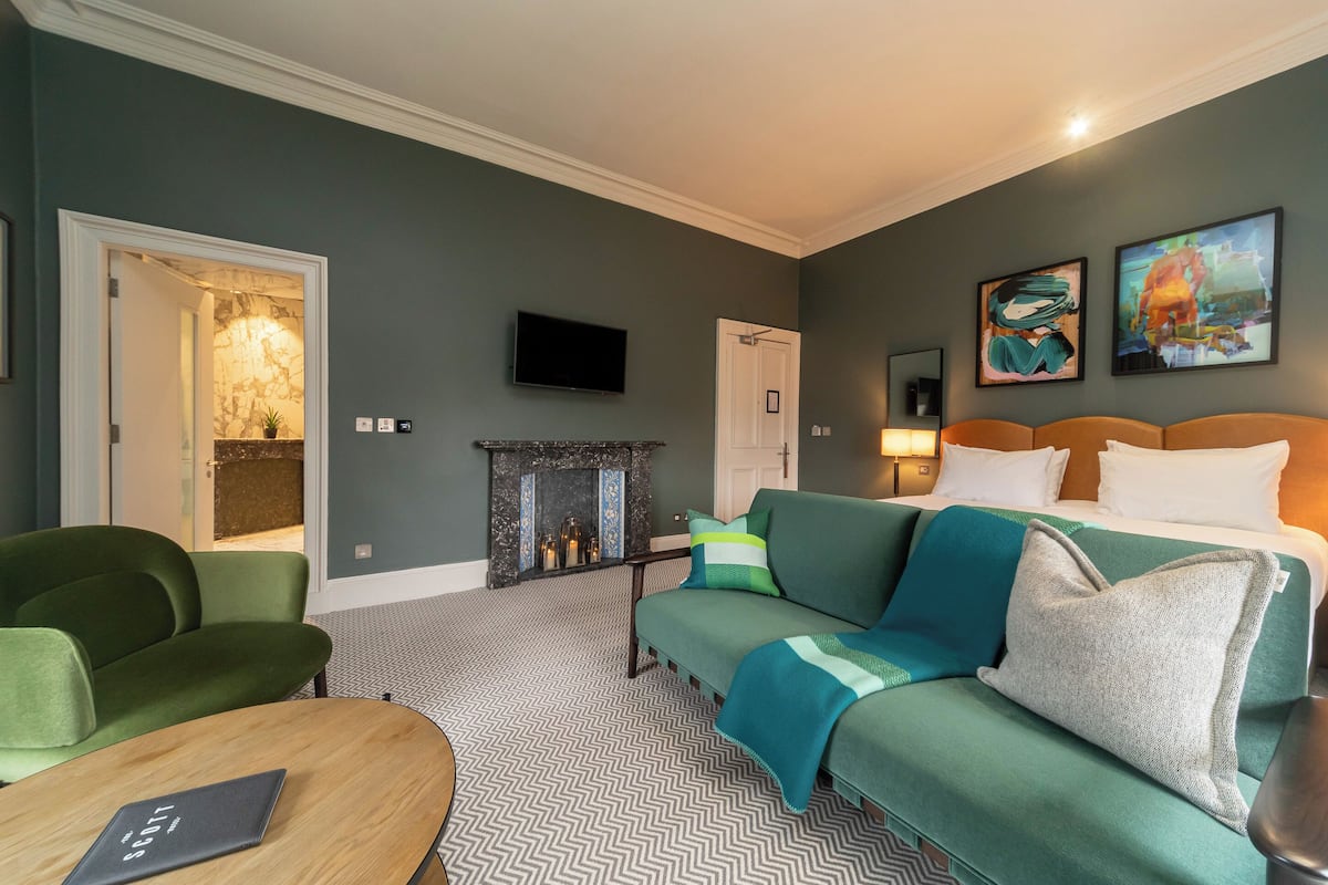 Ein Hotelzimmer mit einem grünen Sofa, einem Holztisch, einem Kamin und einem an der Wand befestigten Fernseher.