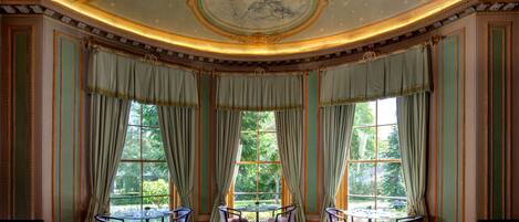 A formal dining room with a large table, chairs, and a view of the outdoors through large windows.