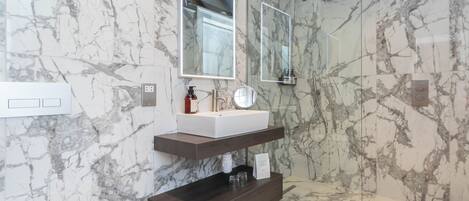 A modern bathroom with a marble backsplash, a built-in sink, a vanity, a toilet, and a shower area.