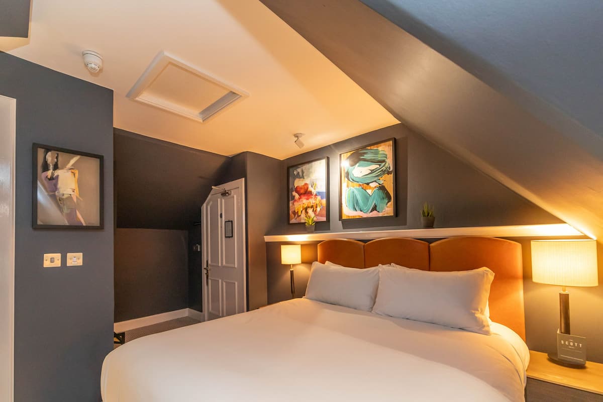 Ein Hotelzimmer mit einem großen Bett, einem Kopfteil, einem Nachttisch, einer Lampe und zwei Bildern an der Wand.