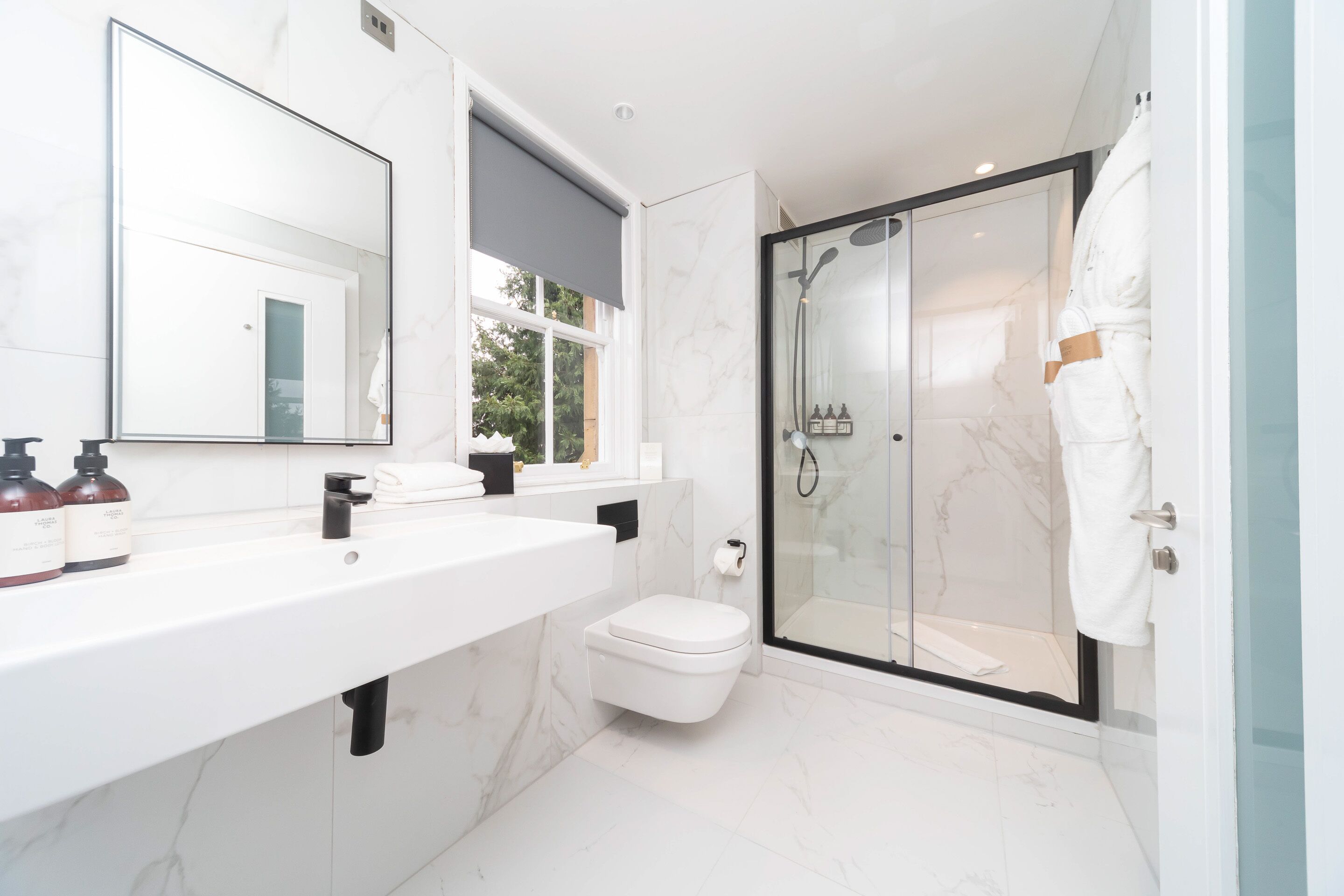 A modern bathroom with a large mirror, white marble tiles, a white sink, and a glass-enclosed shower.