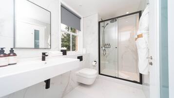 A modern bathroom with a large mirror, white marble tiles, a white sink, and a glass-enclosed shower.