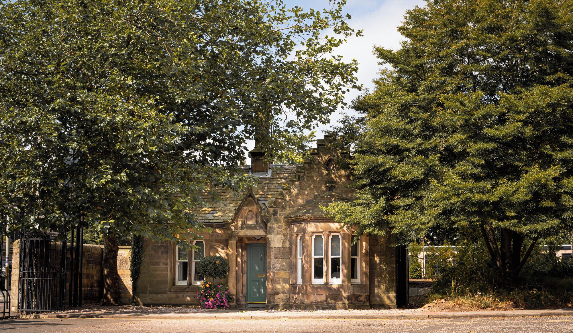 A stone building with a green door and two windows, surrounded by trees.