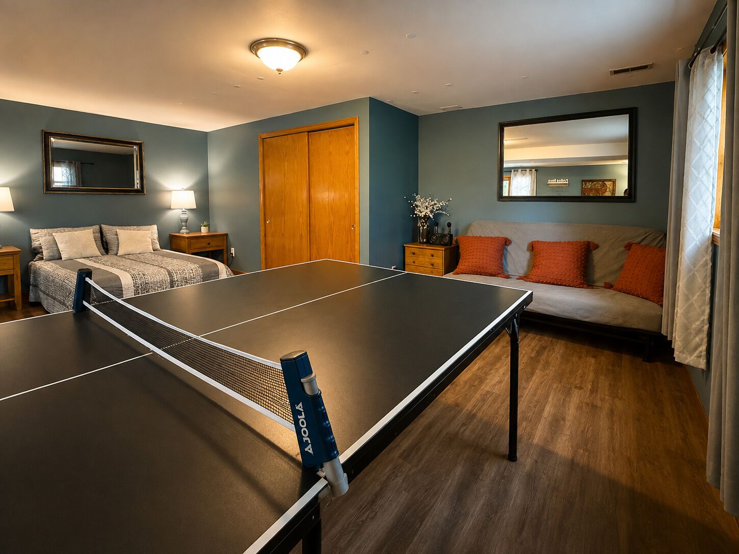 A bedroom with a ping pong table, a bed, a nightstand, a dresser, and a mirror.