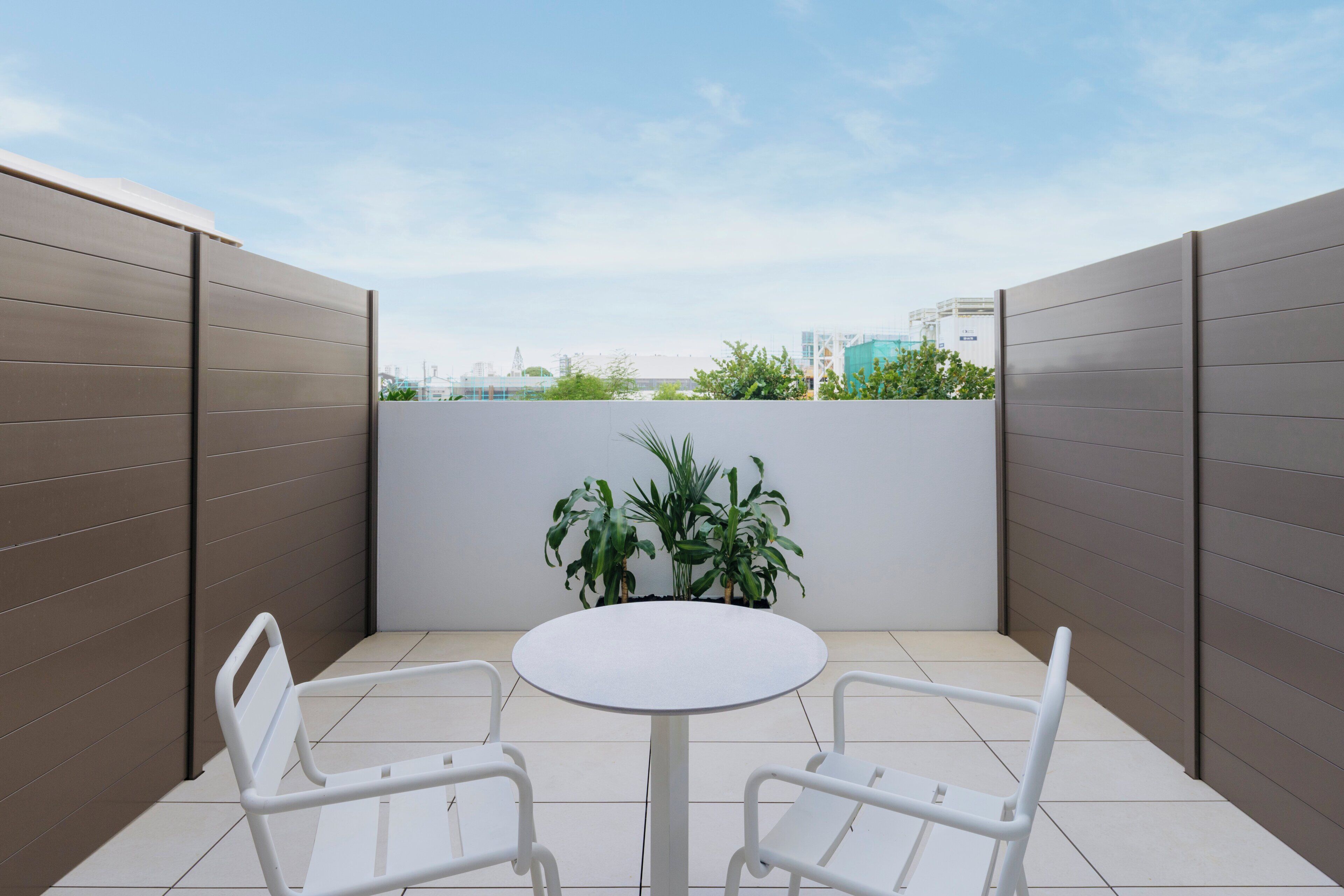 A small, enclosed patio area with a round table and two chairs, surrounded by a low wall and a potted plant.