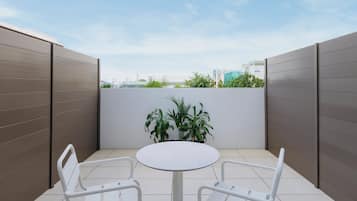 A small, enclosed patio area with a round table and two chairs, surrounded by a low wall and a potted plant.