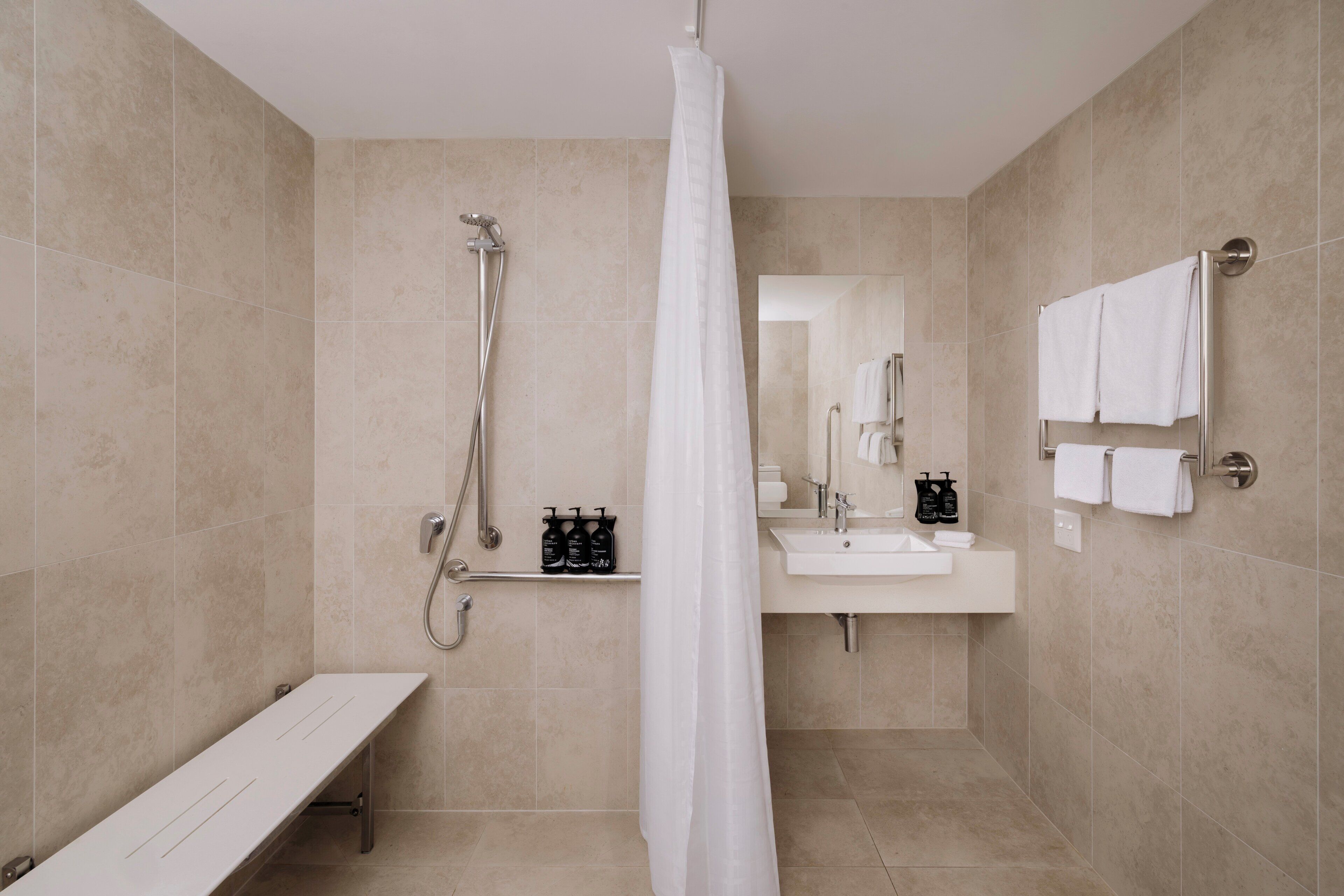 Un baño moderno con ducha, banco, lavamanos y barra para toallas.