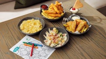 A wooden table with four bowls of food, a coloring book, and crayons.