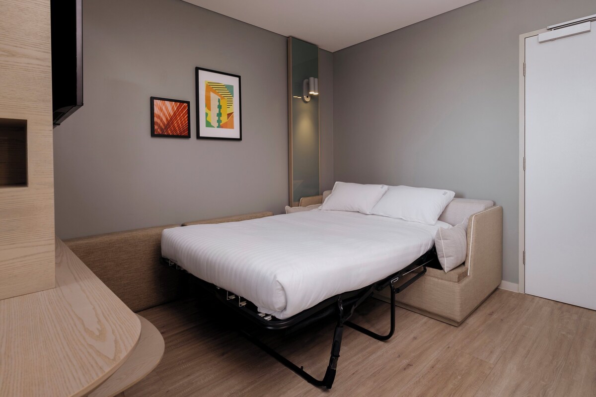 Una habitación moderna con cama, sofá, televisor y obras de arte en la pared.