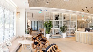 A modern hotel lobby with seating areas, a reception desk, and potted plants.