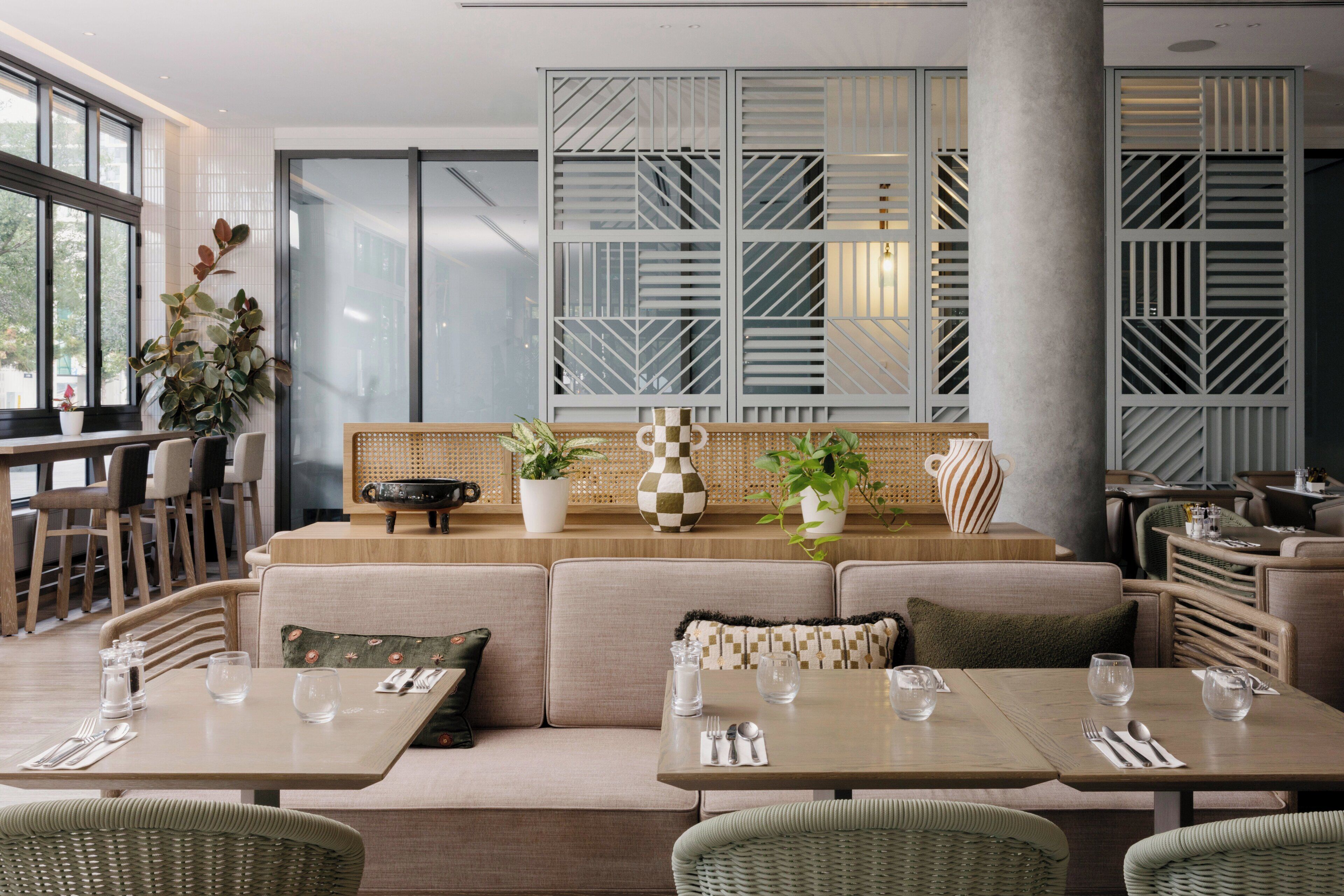 A modern dining area with a long table, cushioned seating, and potted plants.