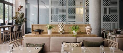 A modern dining area with a long table, cushioned seating, and potted plants.