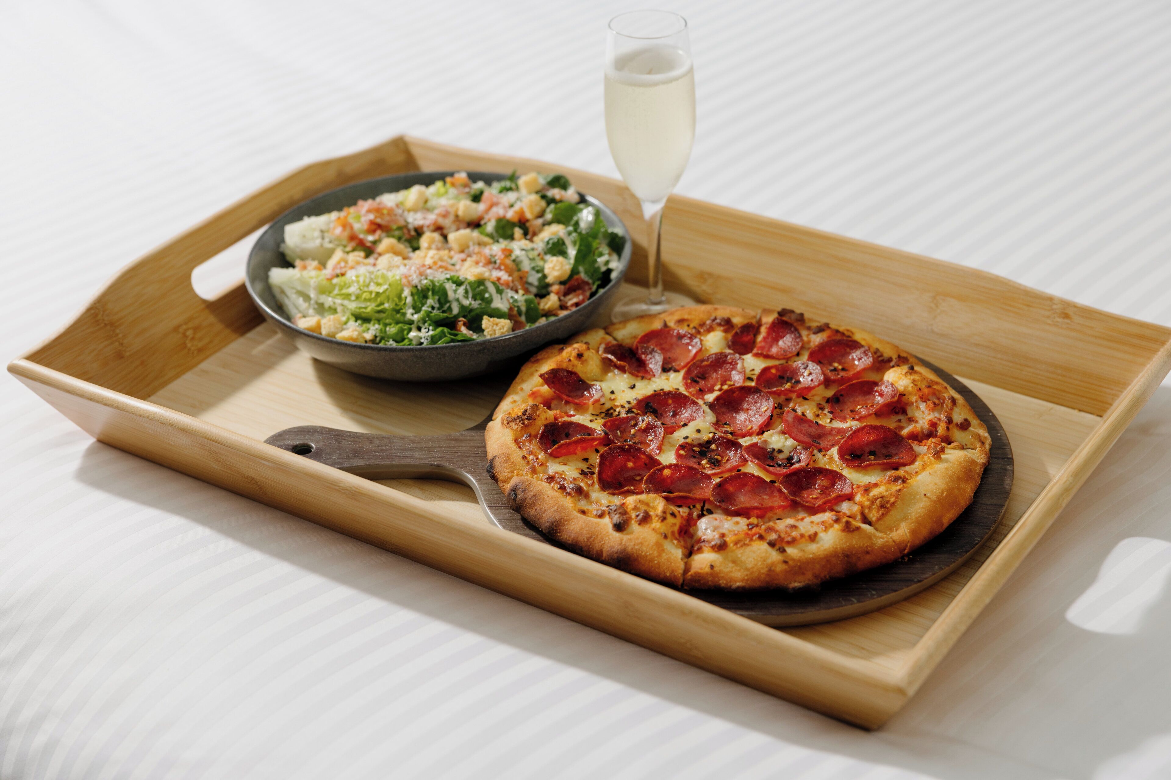 Una bandeja de madera con una pizza y una ensalada sobre una superficie blanca.