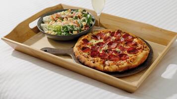 Una bandeja de madera con una pizza y una ensalada sobre una superficie blanca.