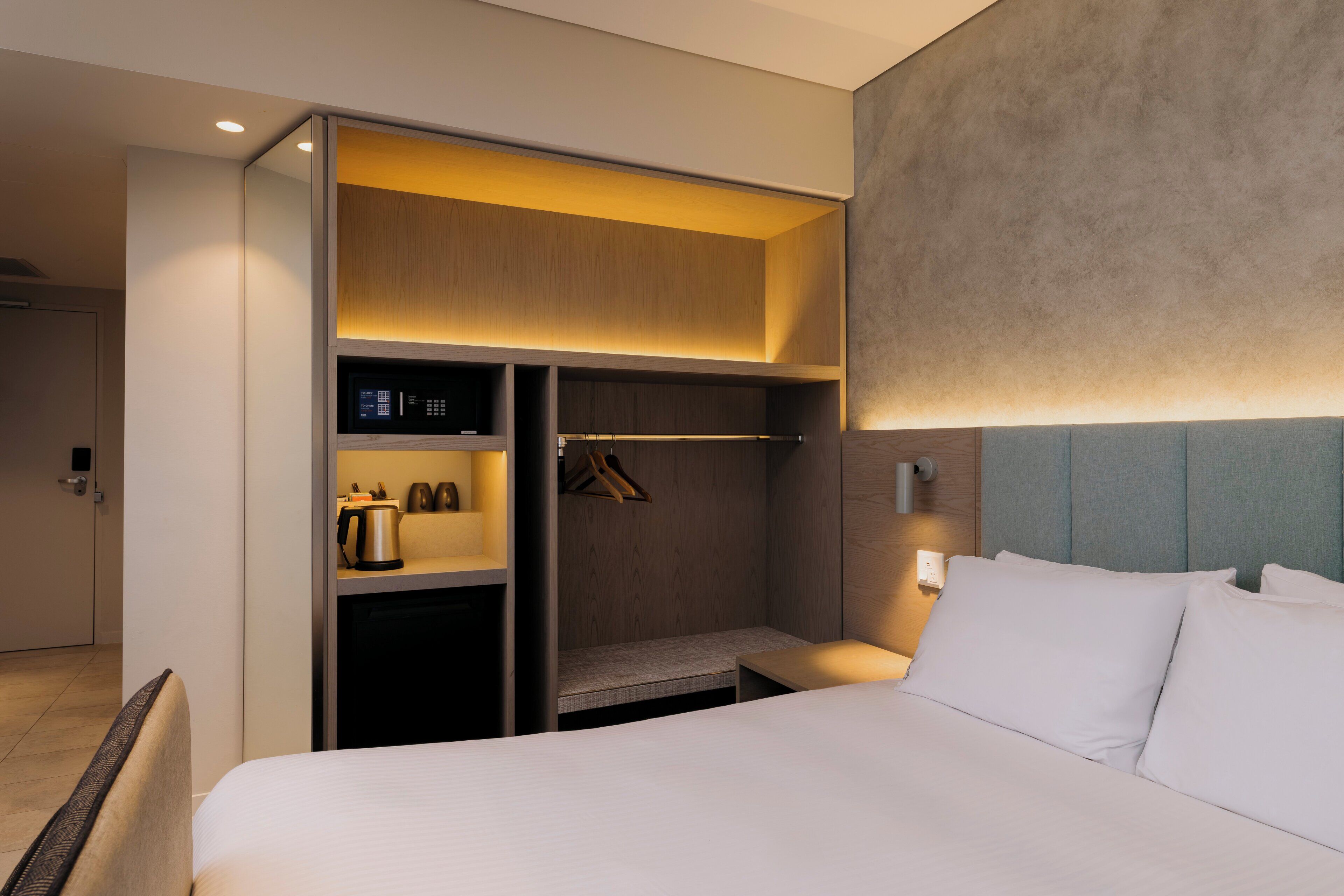 Une chambre d’hôtel comprenant un lit, une armoire, un coin salon et un luminaire fixé au mur.
