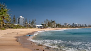 A beach with a sandy shore, clear blue water, and tall buildings in the background.