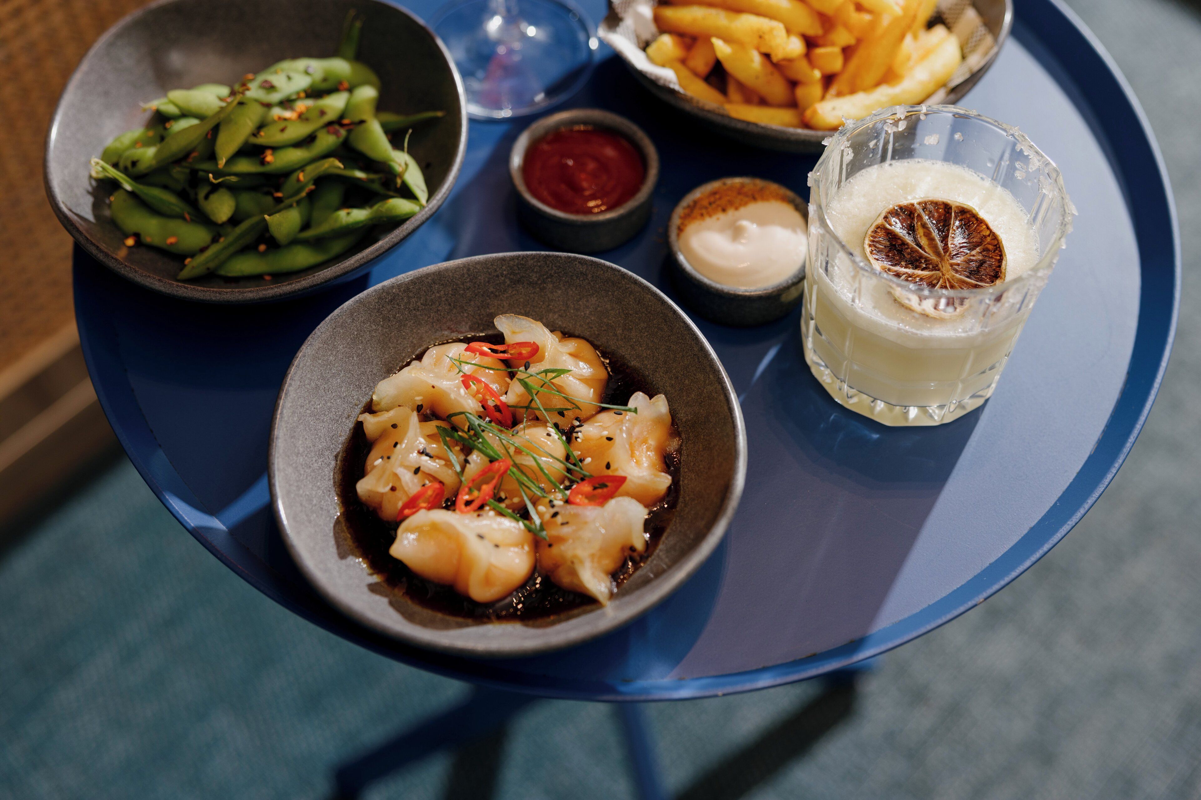 A meal tray with a variety of dishes including dumplings, French fries, edamame, and a glass of a light-colored beverage.