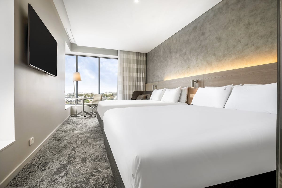 Hotellihuone, jossa on kaksi sänkyä, taulutelevisio, työpöytä lampun kanssa ja näkymä kaupunkiin.