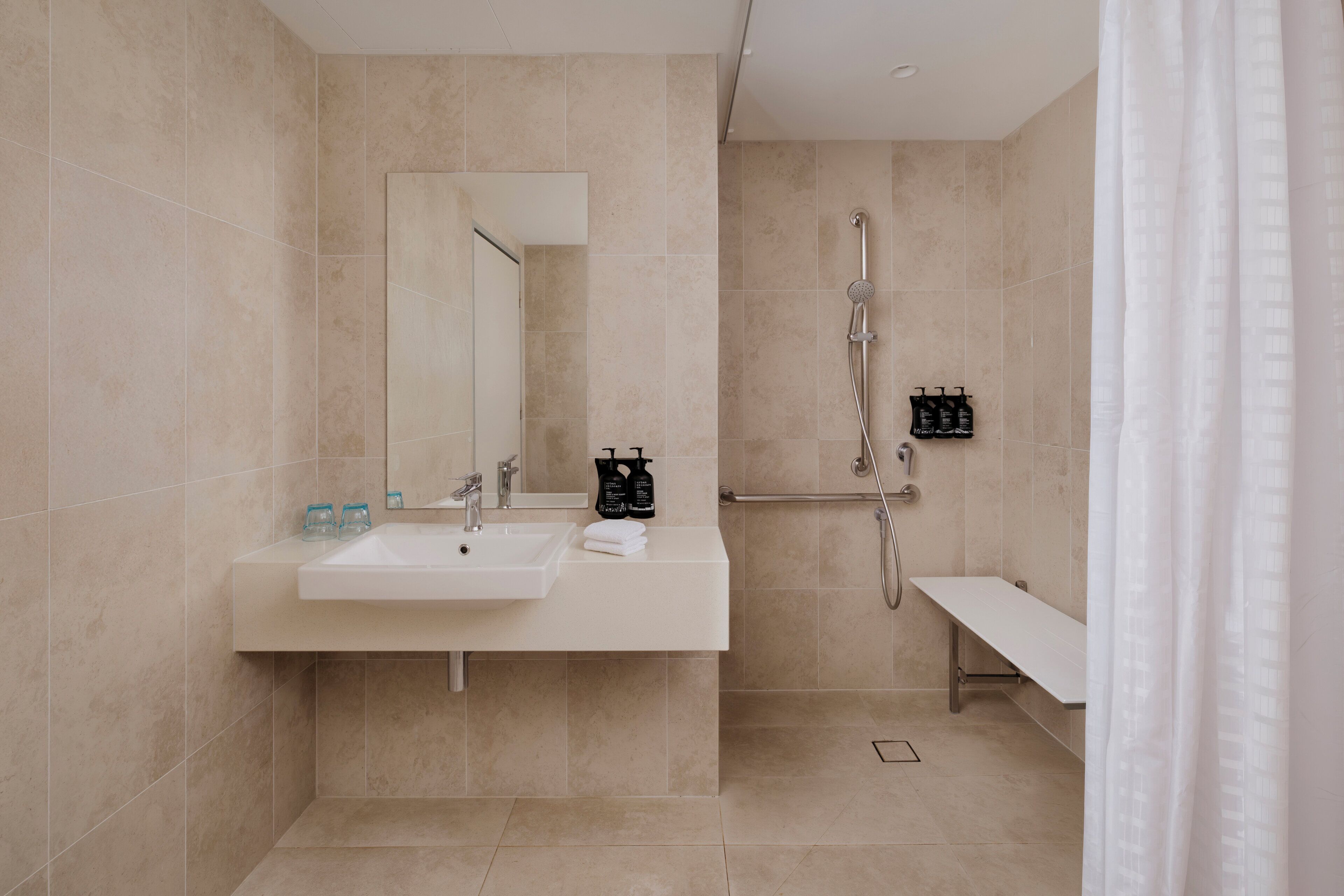 A modern bathroom with a sink, mirror, shower, and bench.
