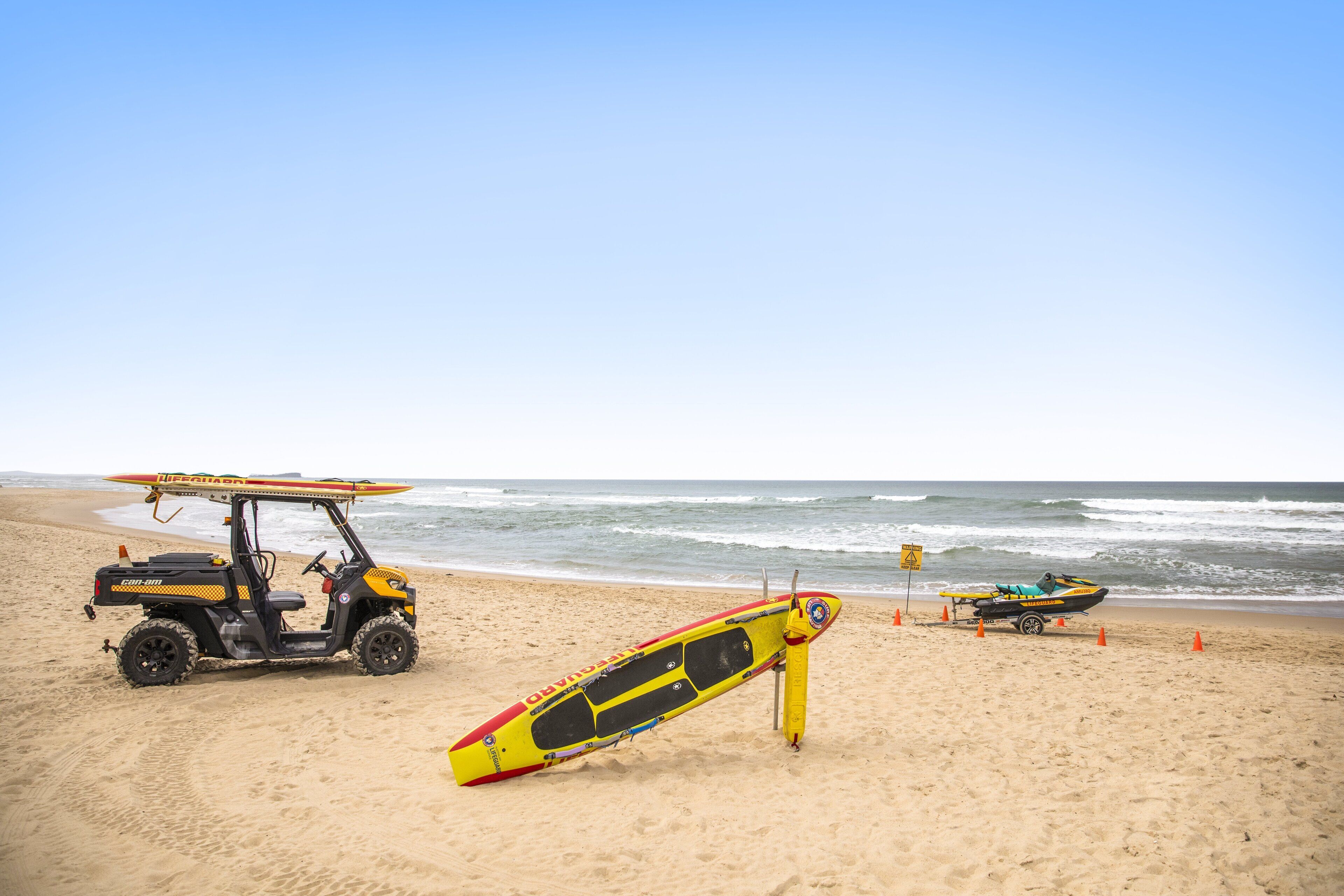 A lifeguard stand with a surfboard and a small boat on a sandy beach.