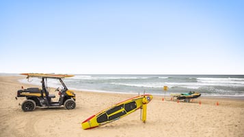 A lifeguard stand with a surfboard and a small boat on a sandy beach.