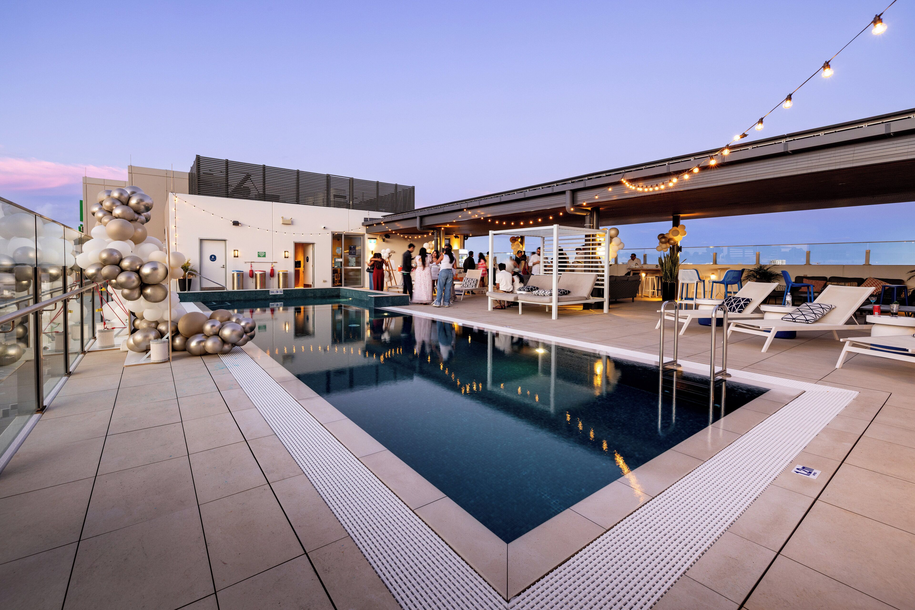 A rooftop pool area with a clear view of the city skyline, a seating area with lounge chairs, and a bar under a covered section.