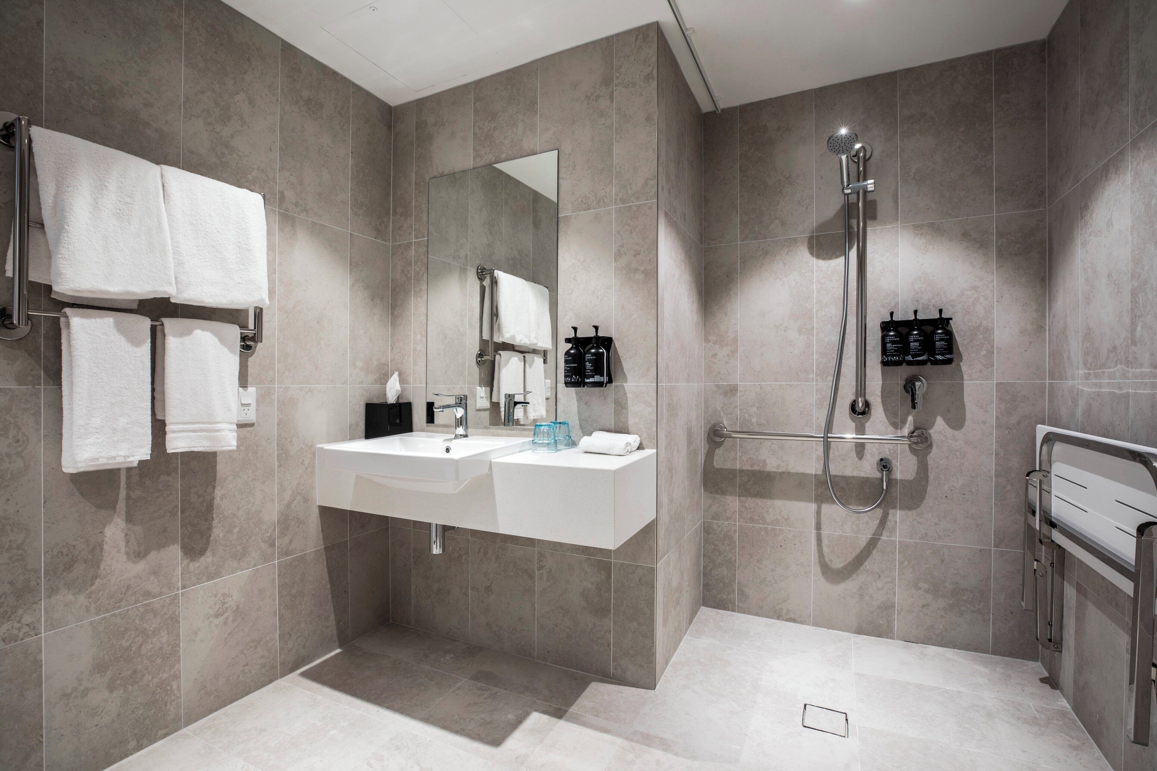 Un baño moderno con lavamanos, espejo, toallero y ducha.
