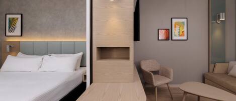 A modern hotel room with a bed, a desk, a chair, a sofa, and a TV mounted on the wall.