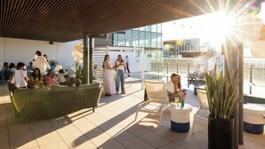 An outdoor seating area with wicker furniture, potted plants, and a view of the cityscape.
