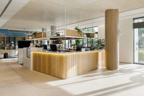 A modern reception area with a wooden reception desk, a large pillar, and a view of the outdoors. - Holiday Inn & Suites Sunshine Coast by IHG (Maroochydore)